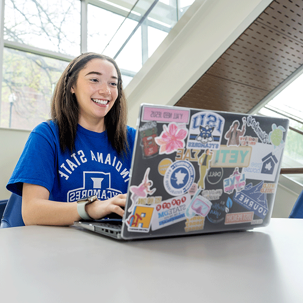 A female student wearing a blue T-shirt types on a laptop which is covered with stickers